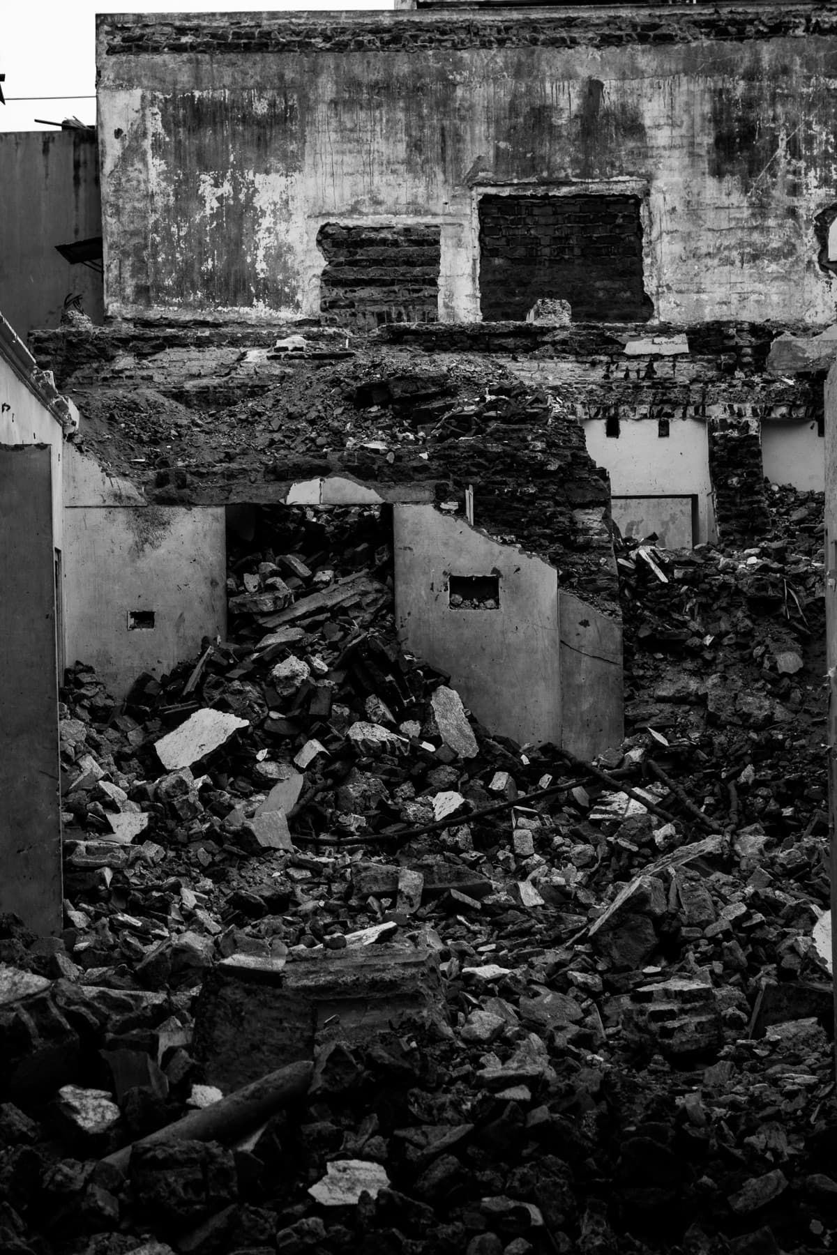 Black and white photo of a half-demolished building, its inner walls standing among piles of rubble